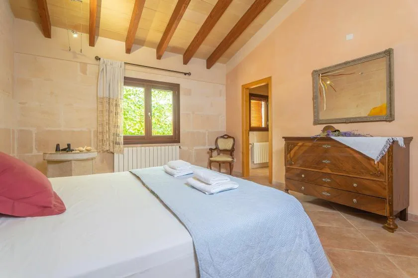 A bedroom with a bed, a window, and a wooden chest of drawers.