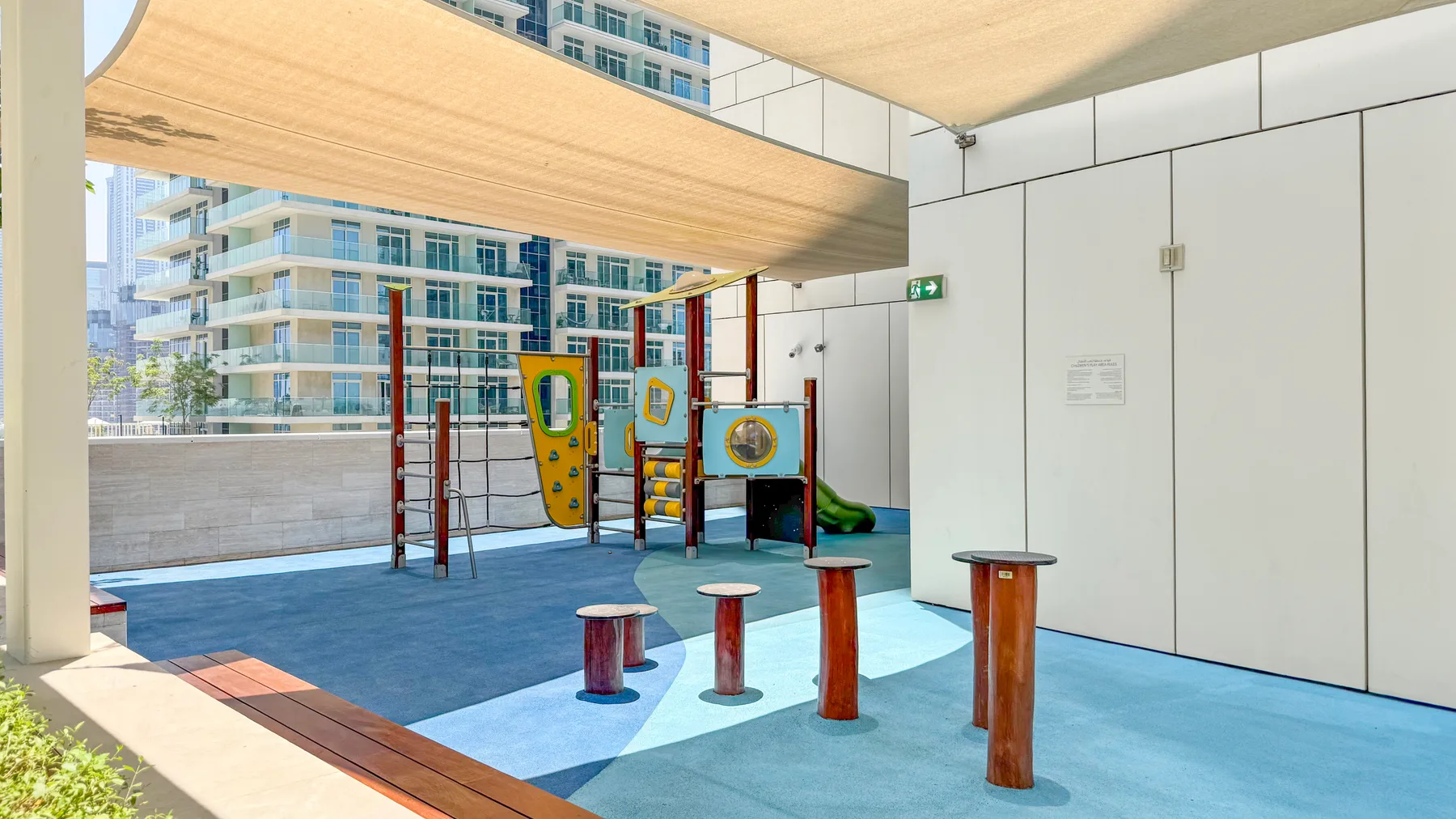 A shaded outdoor play area with colorful climbing equipment and balance posts.