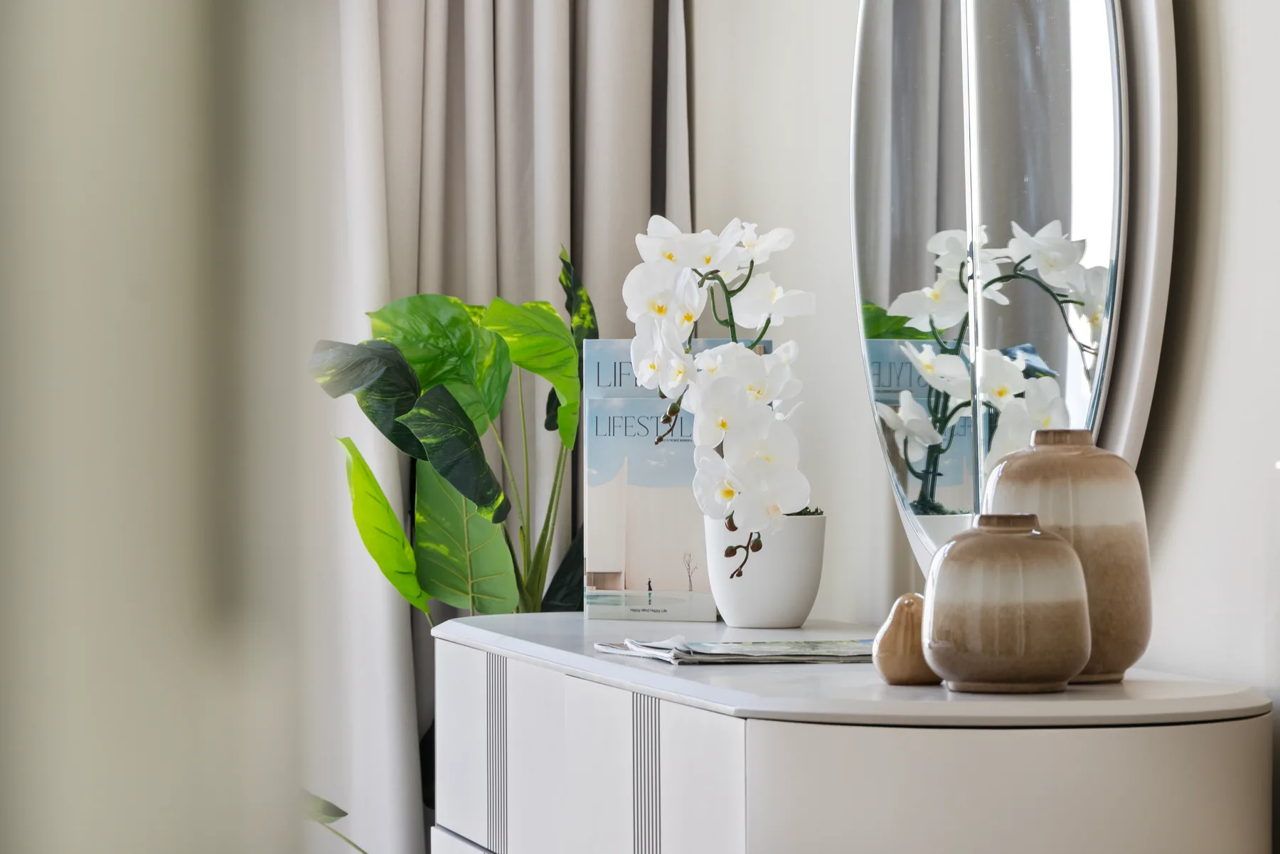 A bright room corner with a white cabinet, leafy plant, and orchids.