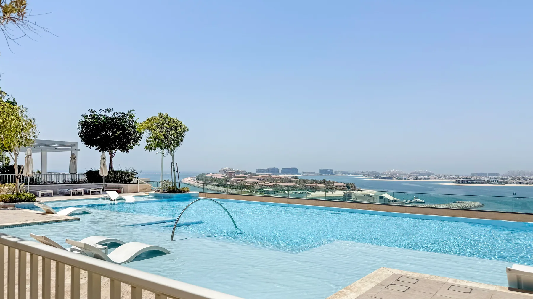 An outdoor swimming pool overlooks the waterfront and distant buildings.