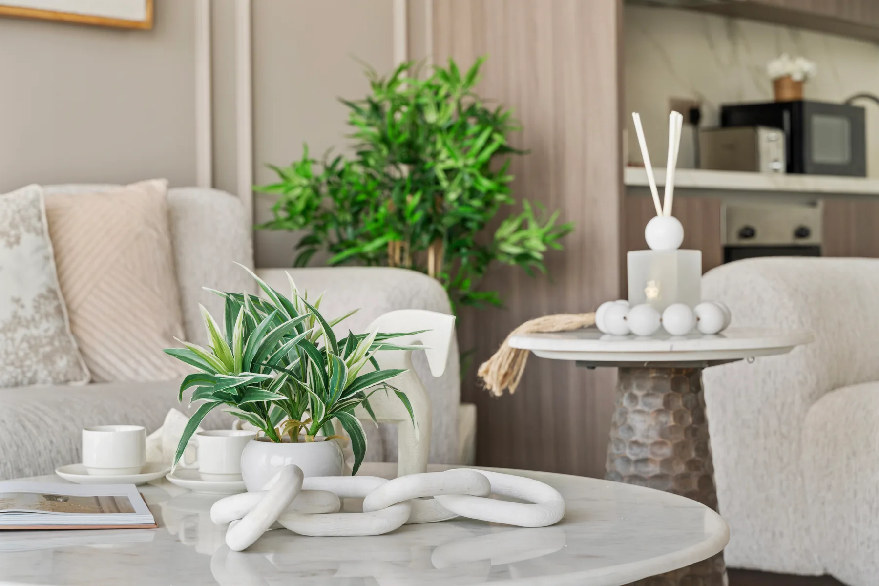 A living room with light seating, a coffee table, and green plants.