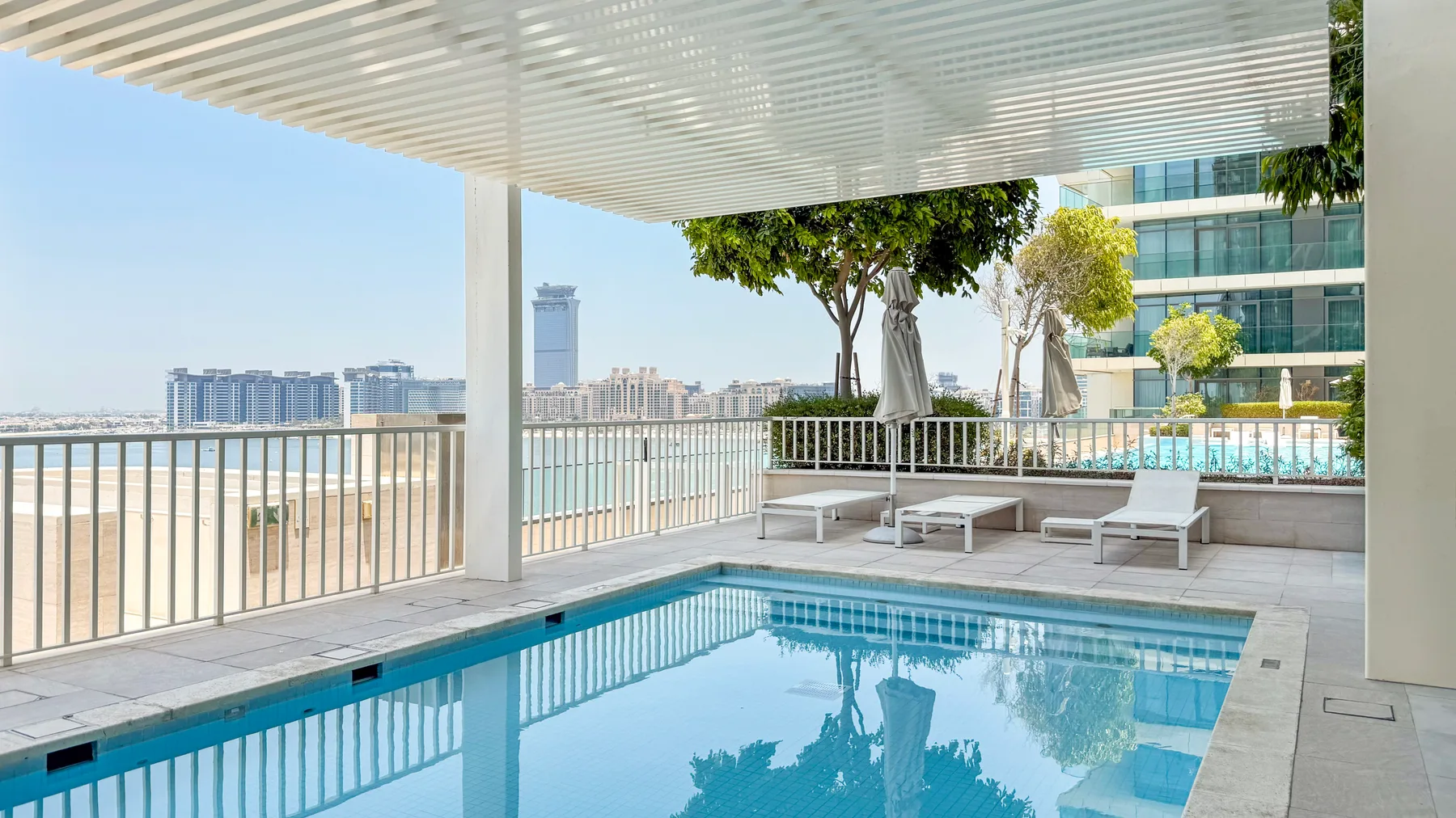 An outdoor swimming pool sits beside a shaded terrace overlooking the water.