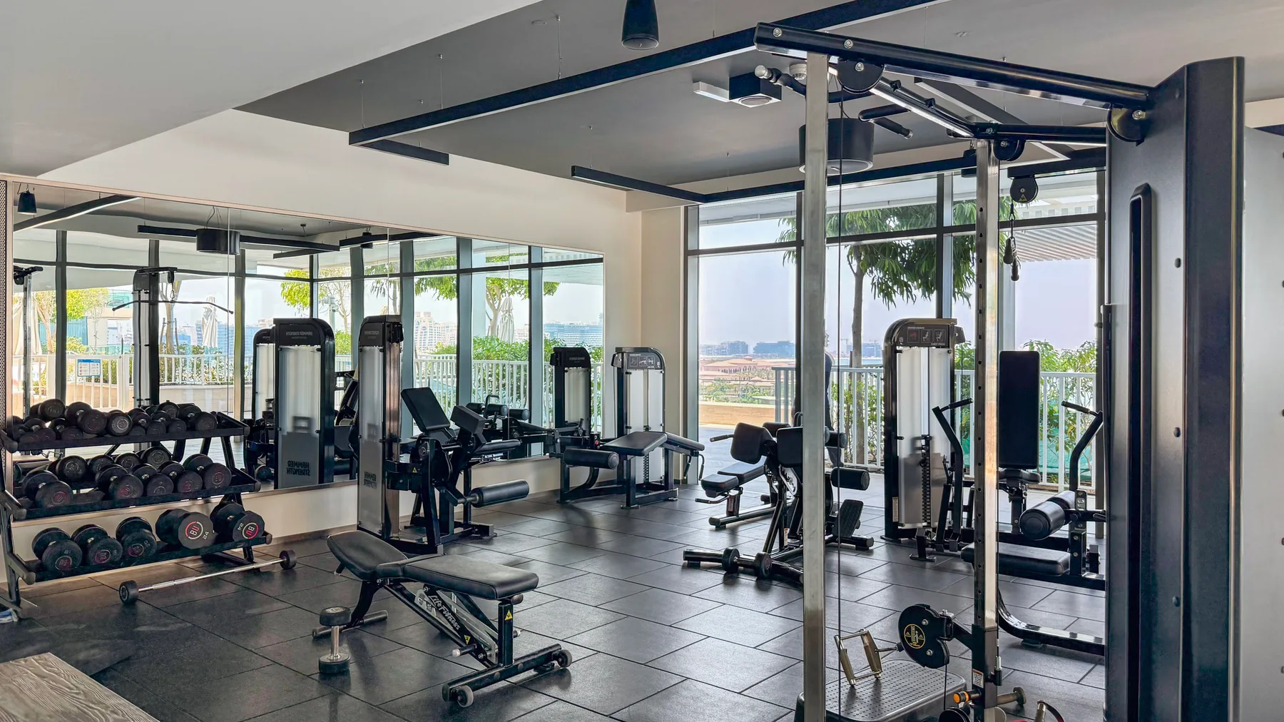A gym with weight racks, exercise machines, and large windows.
