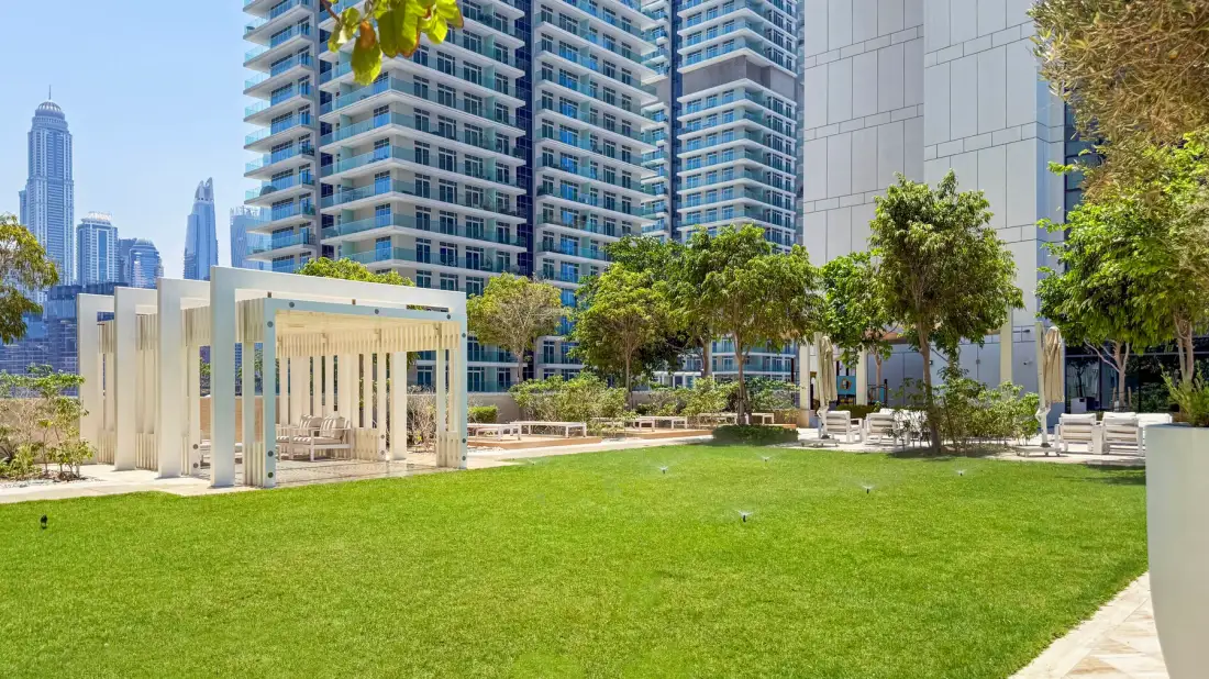 A landscaped courtyard with a broad lawn, trees, and modern high-rise buildings.