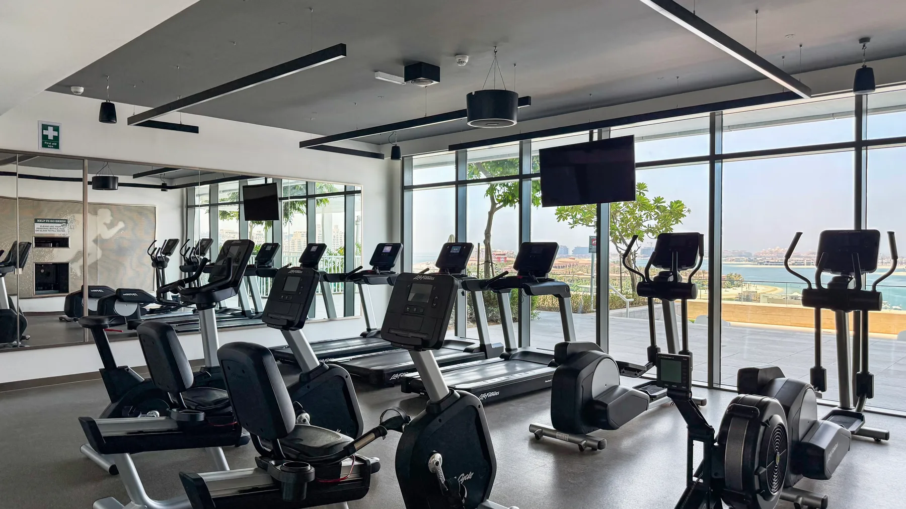 A gym with cardio machines arranged beside large windows.