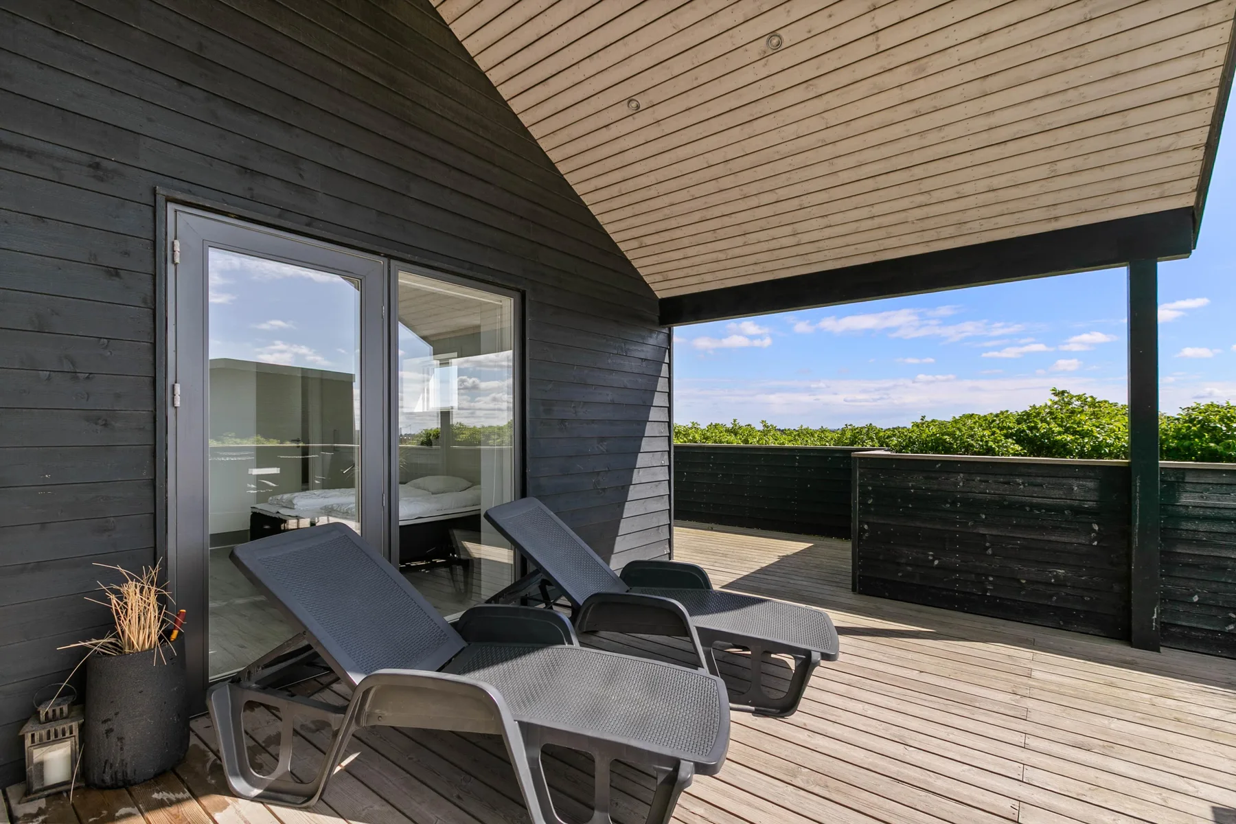 Una terraza de madera cubierta con asientos reclinables da a un seto verde.
