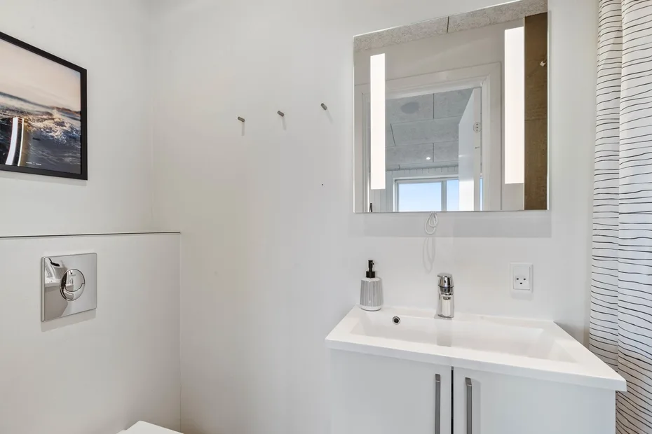 Un baño luminoso con lavabo, espejo y botón de descarga del inodoro.