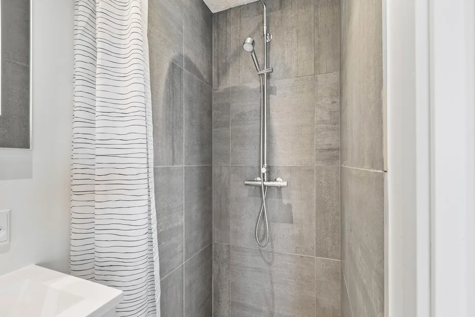 Una ducha con azulejos, ducha de mano y cortina a rayas.