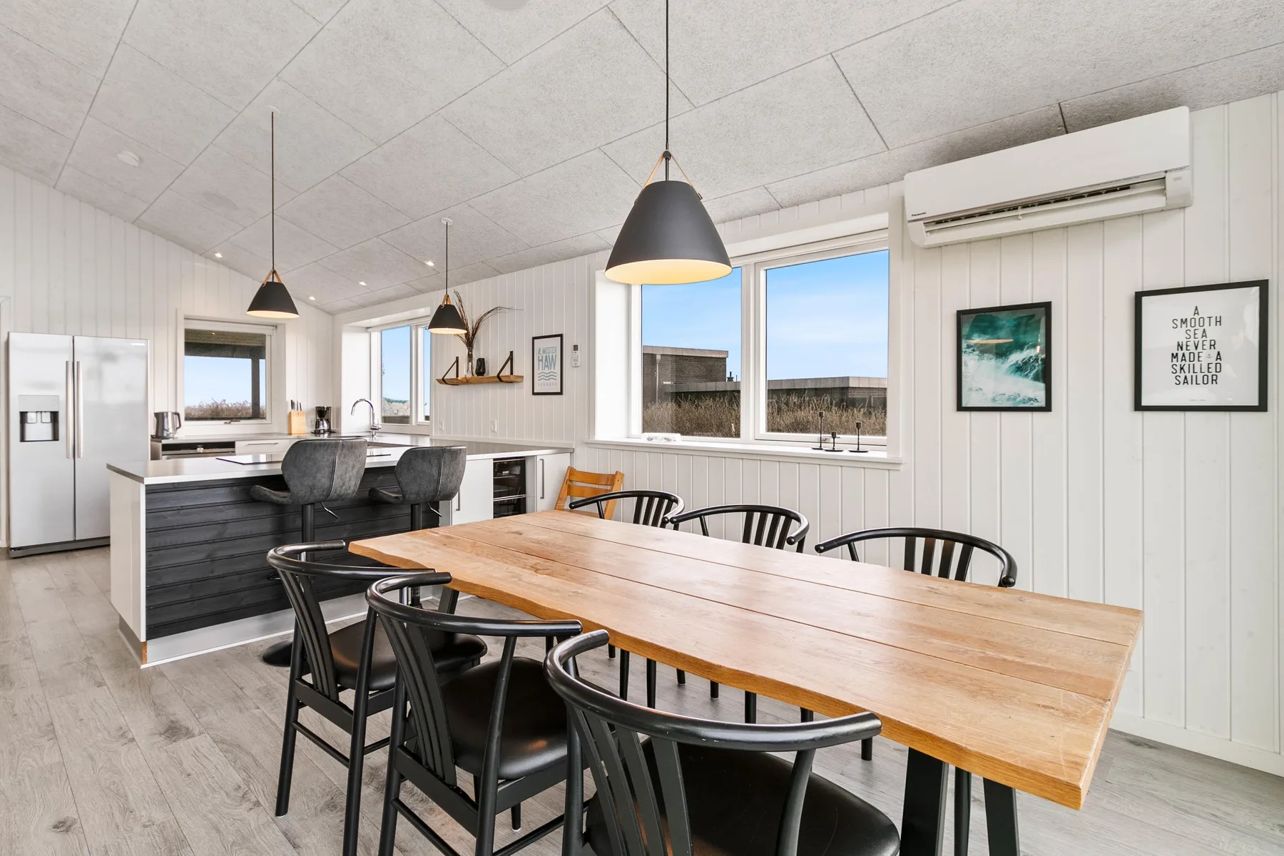 Una cocina luminosa con comedor, una mesa larga de madera y lámparas colgantes.