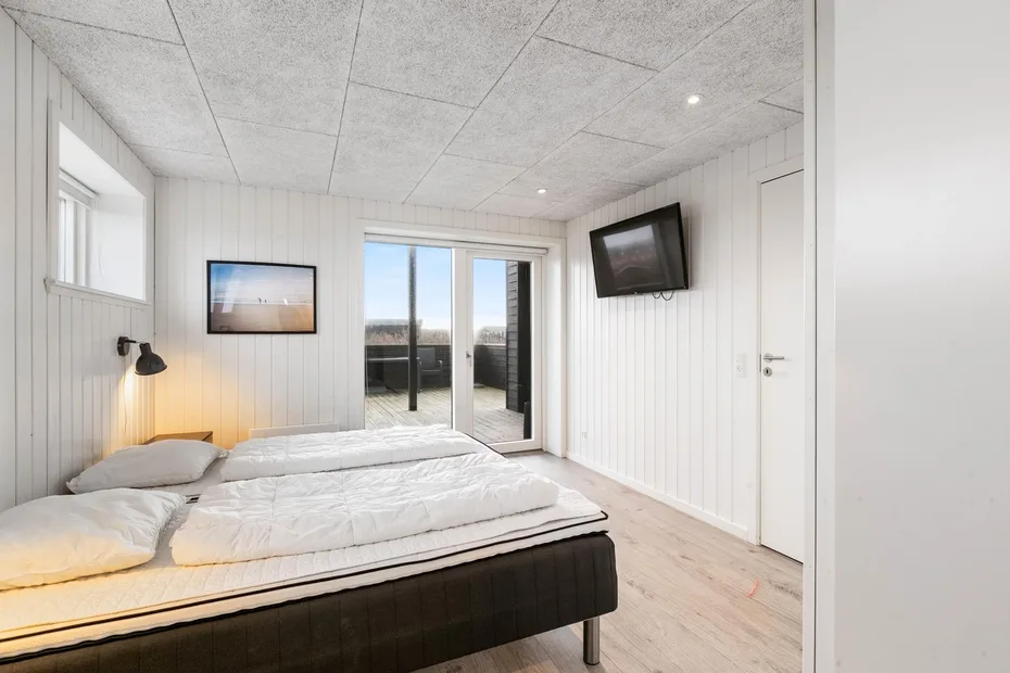 Un dormitorio con una cama, un televisor en la pared y puertas de vidrio que dan a un balcón.