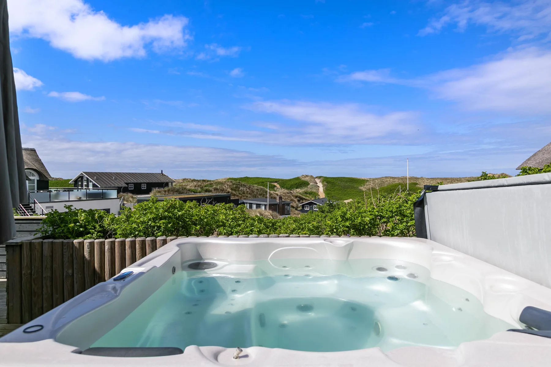 Bañera de hidromasaje al aire libre con vistas a casas cercanas y dunas costeras.