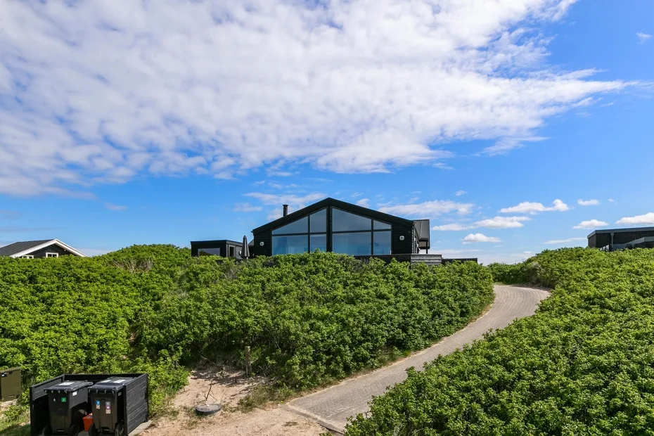 Un edificio moderno con fachada de vidrio se alza tras un sendero y arbustos verdes.