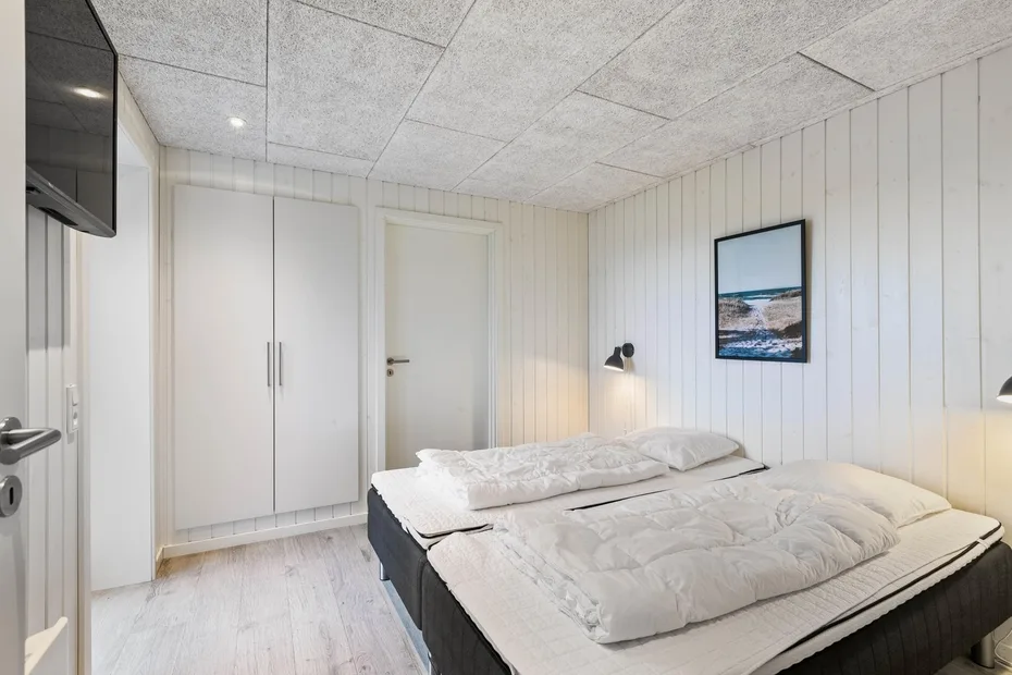 Un dormitorio con una cama doble, ropa de cama blanca y un cuadro en la pared.