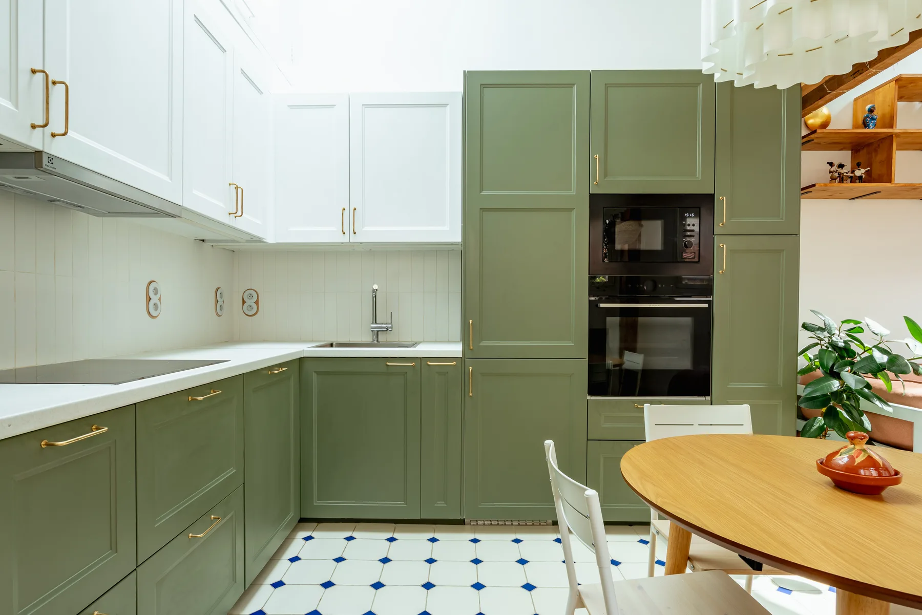Una cocina luminosa con gabinetes verdes, encimeras blancas y una mesa redonda.