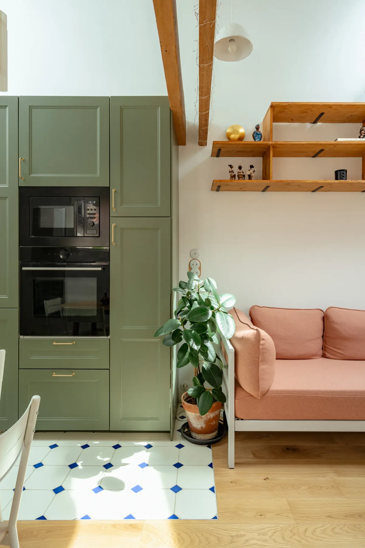 Una cocina con armarios verdes y horno empotrado junto a una zona de estar.