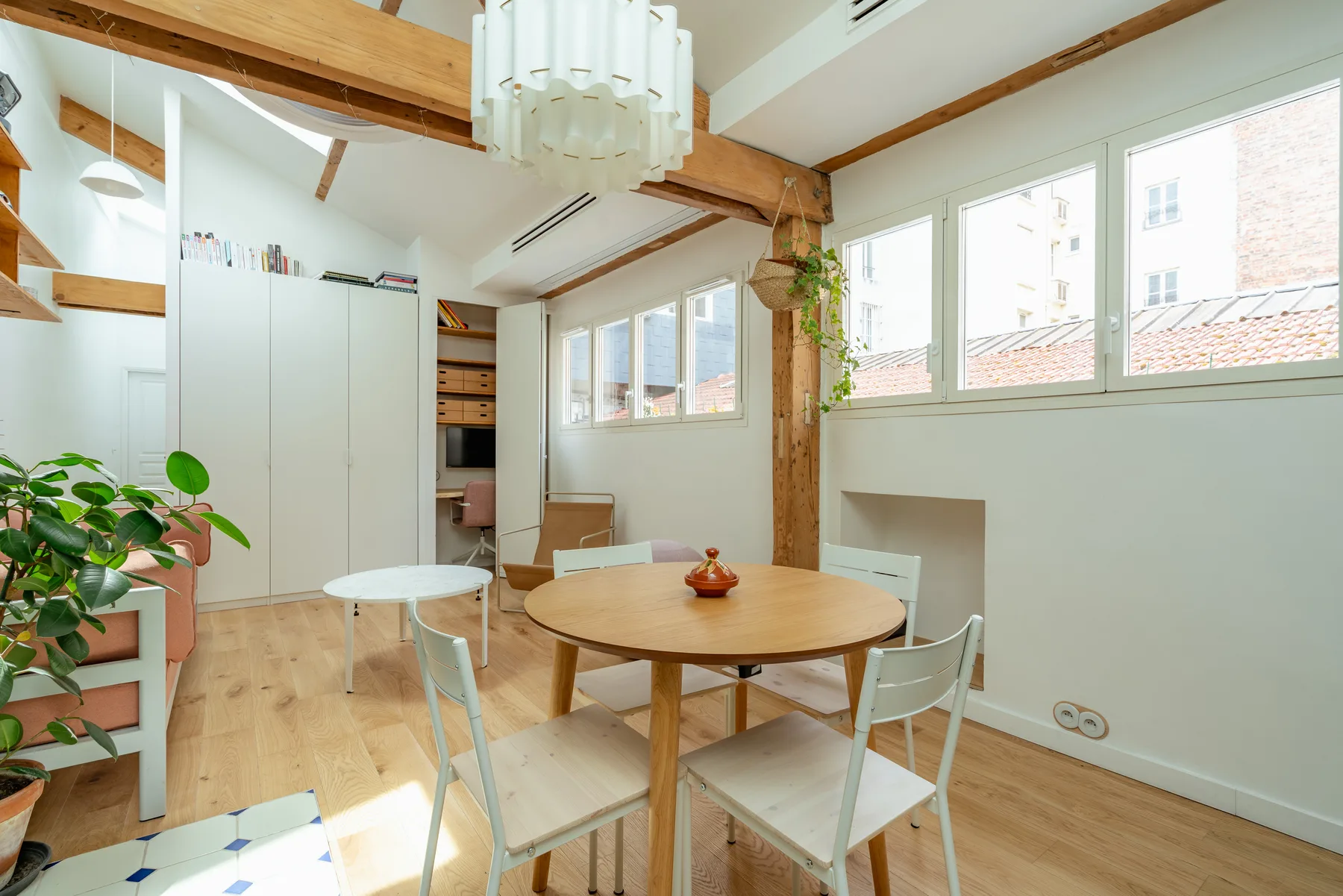 Un comedor luminoso con una mesa redonda de madera, sillas y ventanas grandes.