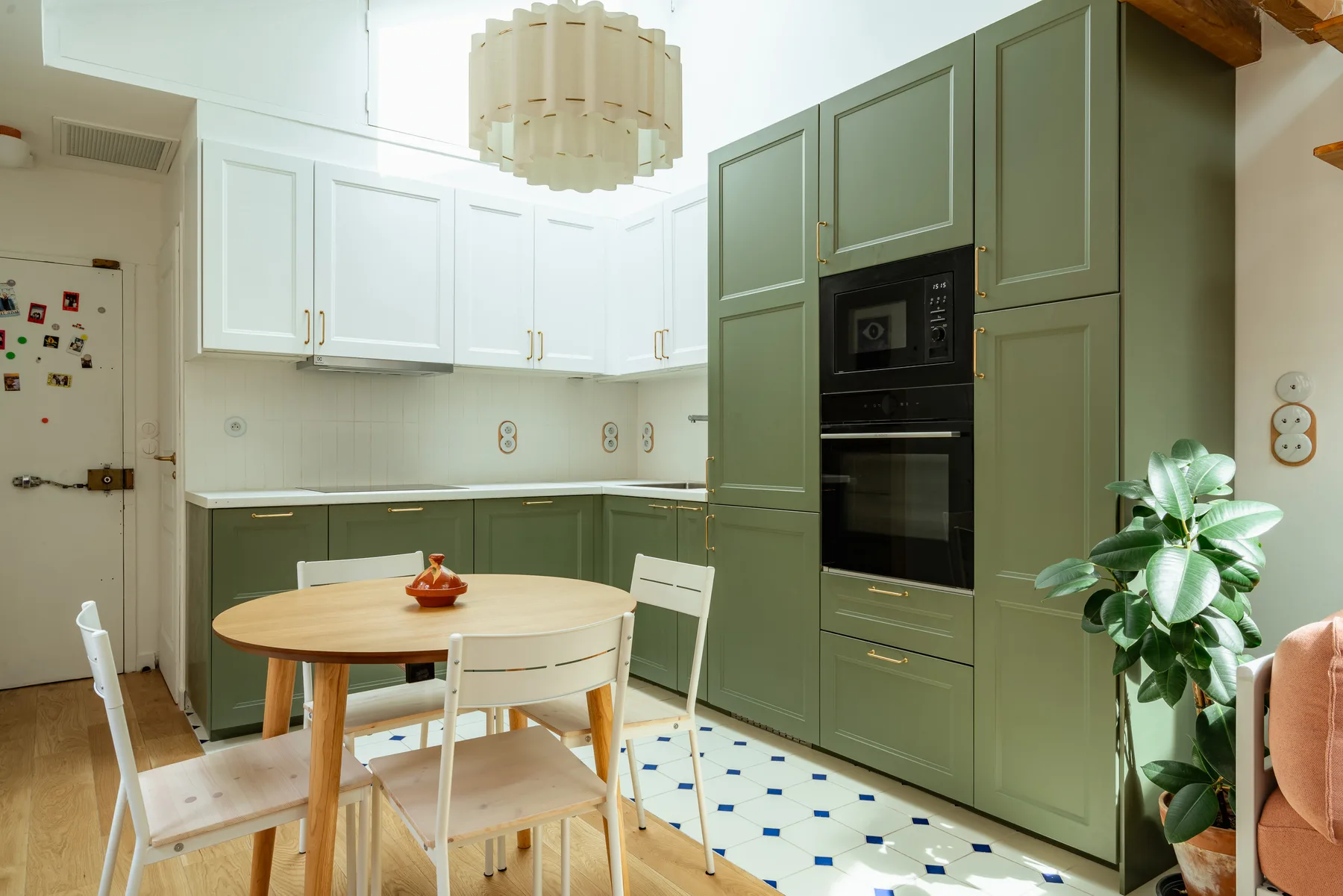 Una cocina luminosa con gabinetes verdes, una mesa de comedor y una planta en maceta.