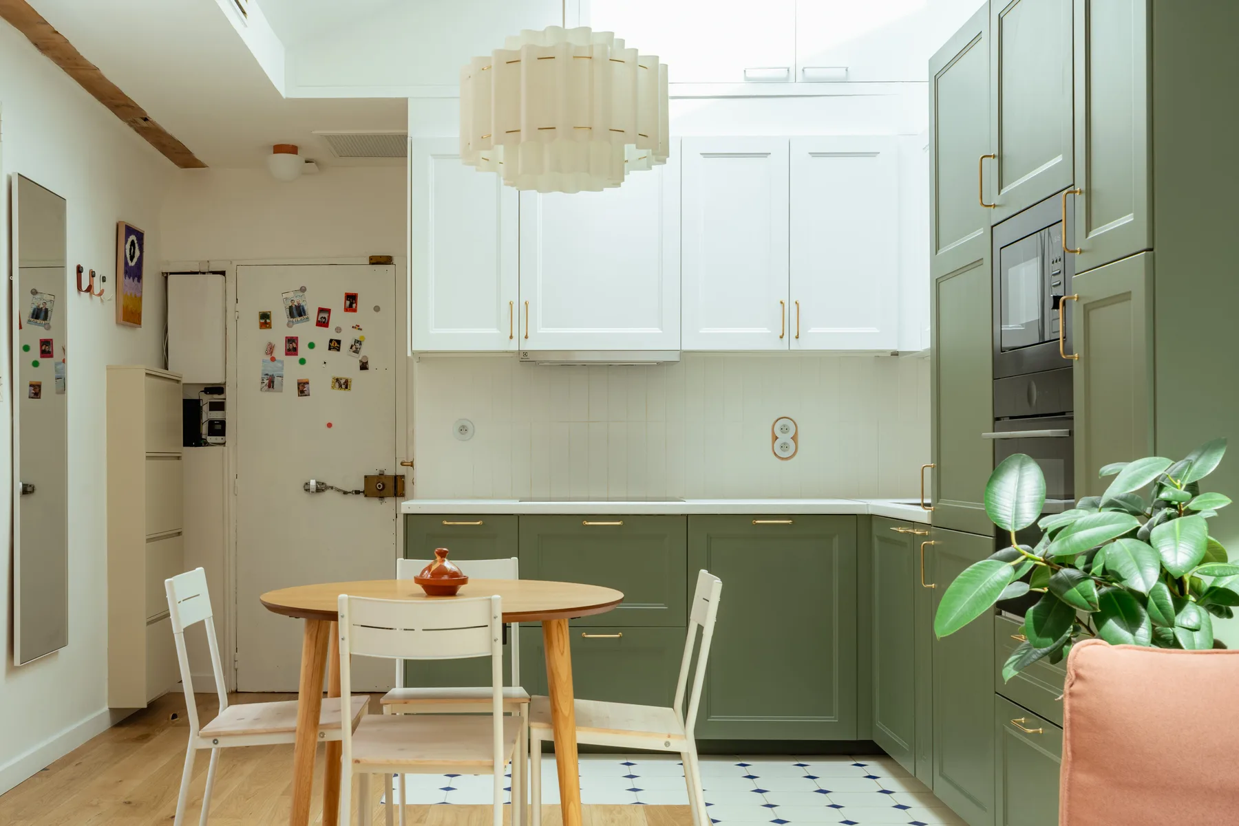 Una cocina luminosa con gabinetes blancos arriba, gabinetes verdes abajo y una pequeña mesa de comedor.
