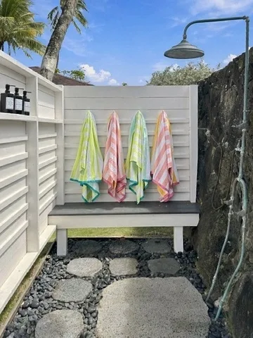 Zona de ducha al aire libre con toallas de colores colgadas en una pared blanca.