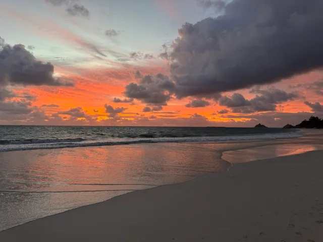 Una playa al atardecer, con luz naranja reflejada en el agua poco profunda.