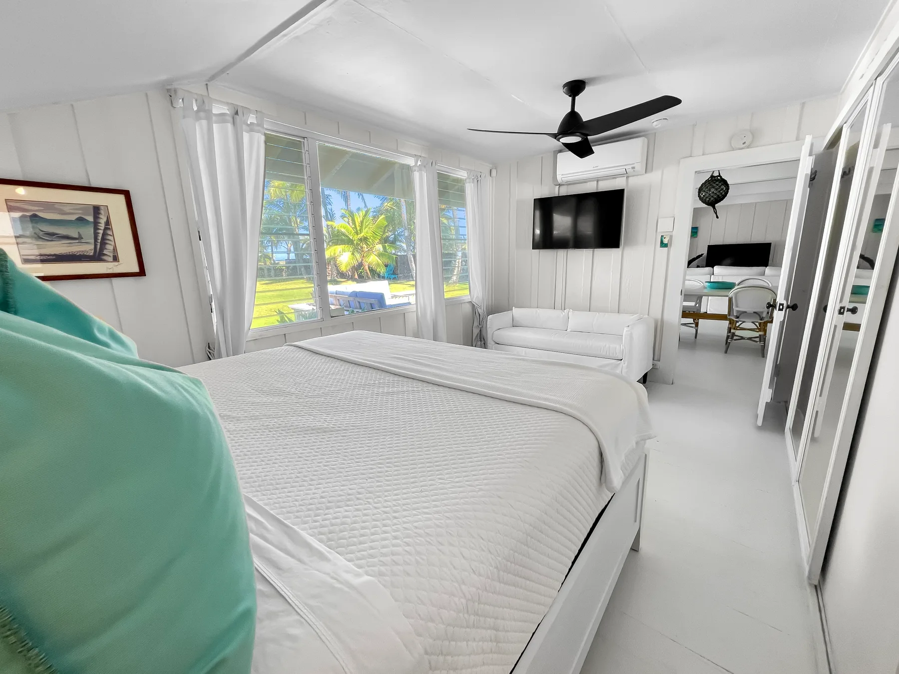 Un dormitorio luminoso con una cama grande, ventanas y un ventilador de techo.