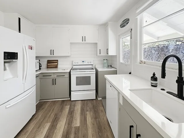 Una cocina luminosa con gabinetes blancos, una estufa y un fregadero grande.