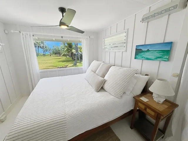 Un dormitorio luminoso con una cama blanca y una ventana con vista a la vegetación.