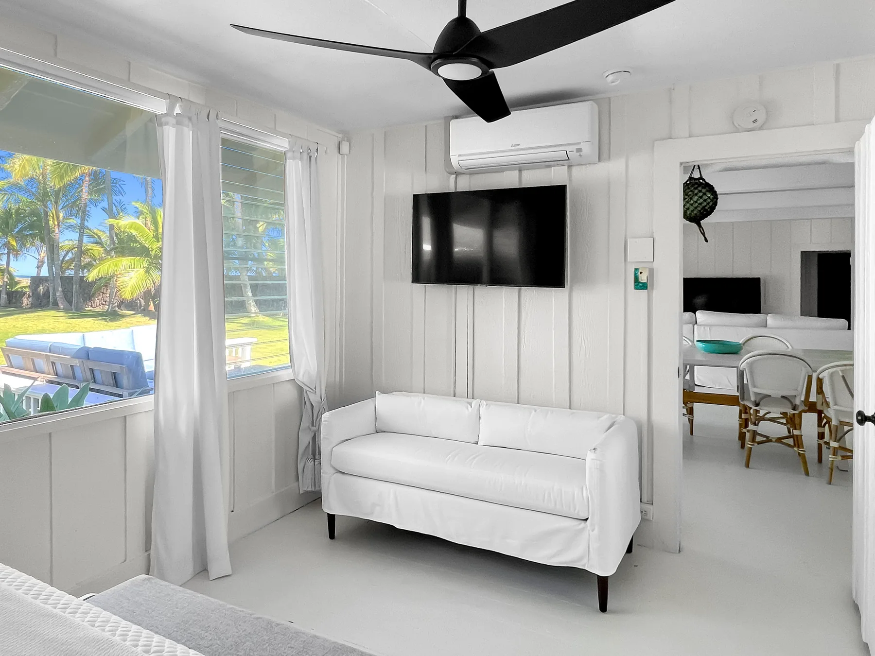 Una sala luminosa con asientos blancos y un televisor en la pared junto a grandes ventanas.