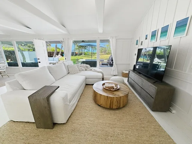 Una sala luminosa con asientos blancos, una mesa de centro redonda de madera y grandes ventanas.