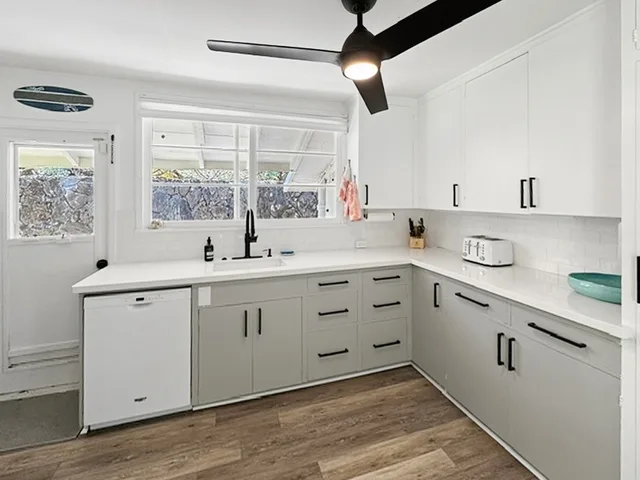 Una cocina luminosa con gabinetes blancos, piso de madera y una ventana sobre el fregadero.