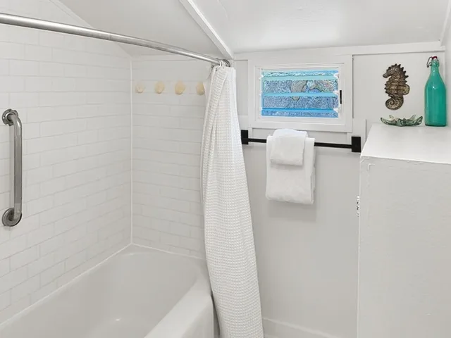 Un baño luminoso con bañera, paredes de azulejos blancos y una ventana pequeña.