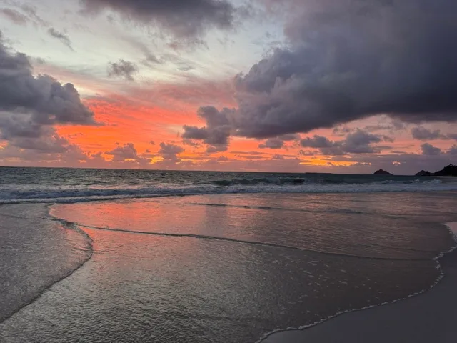 Una playa al atardecer, con nubes coloridas reflejadas en la arena mojada.