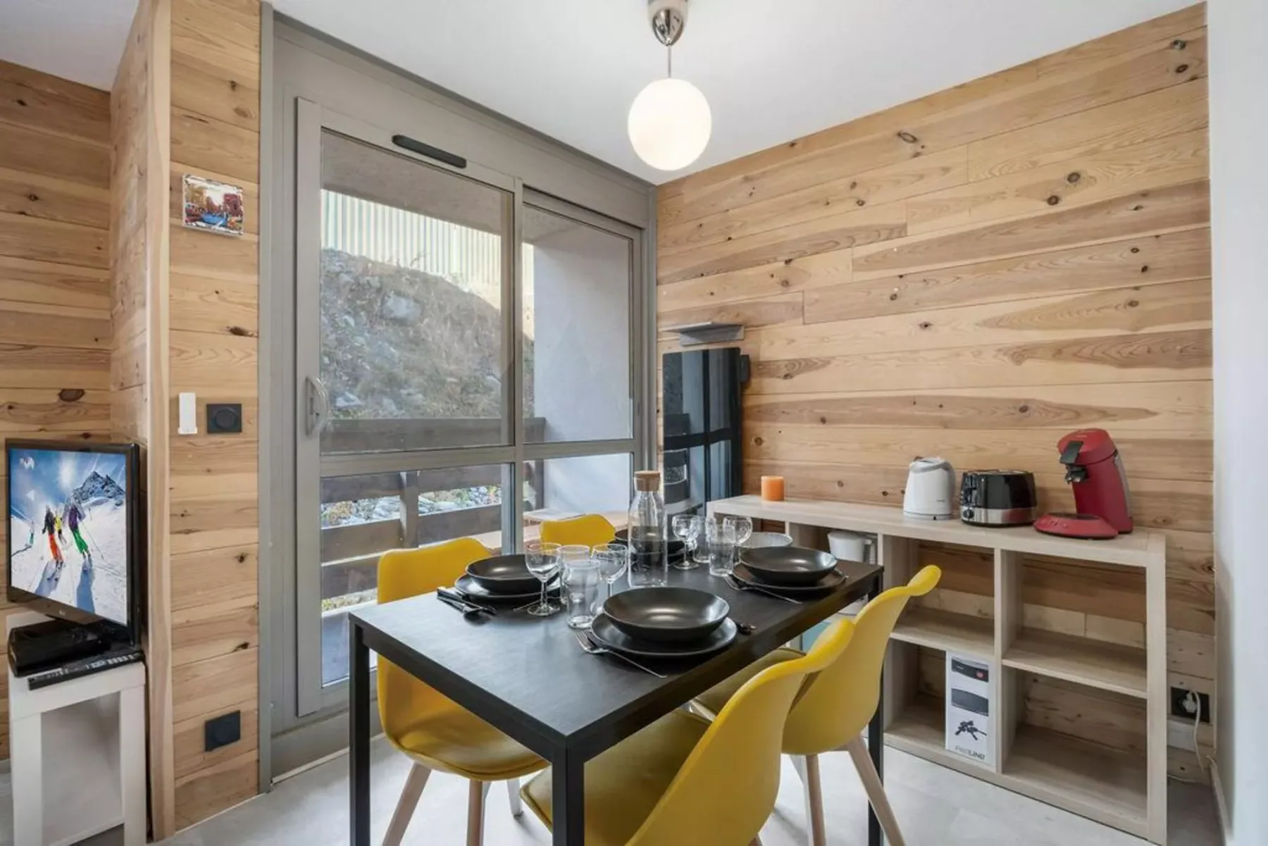 Un comedor con la mesa puesta, asientos amarillos y paredes revestidas de madera.