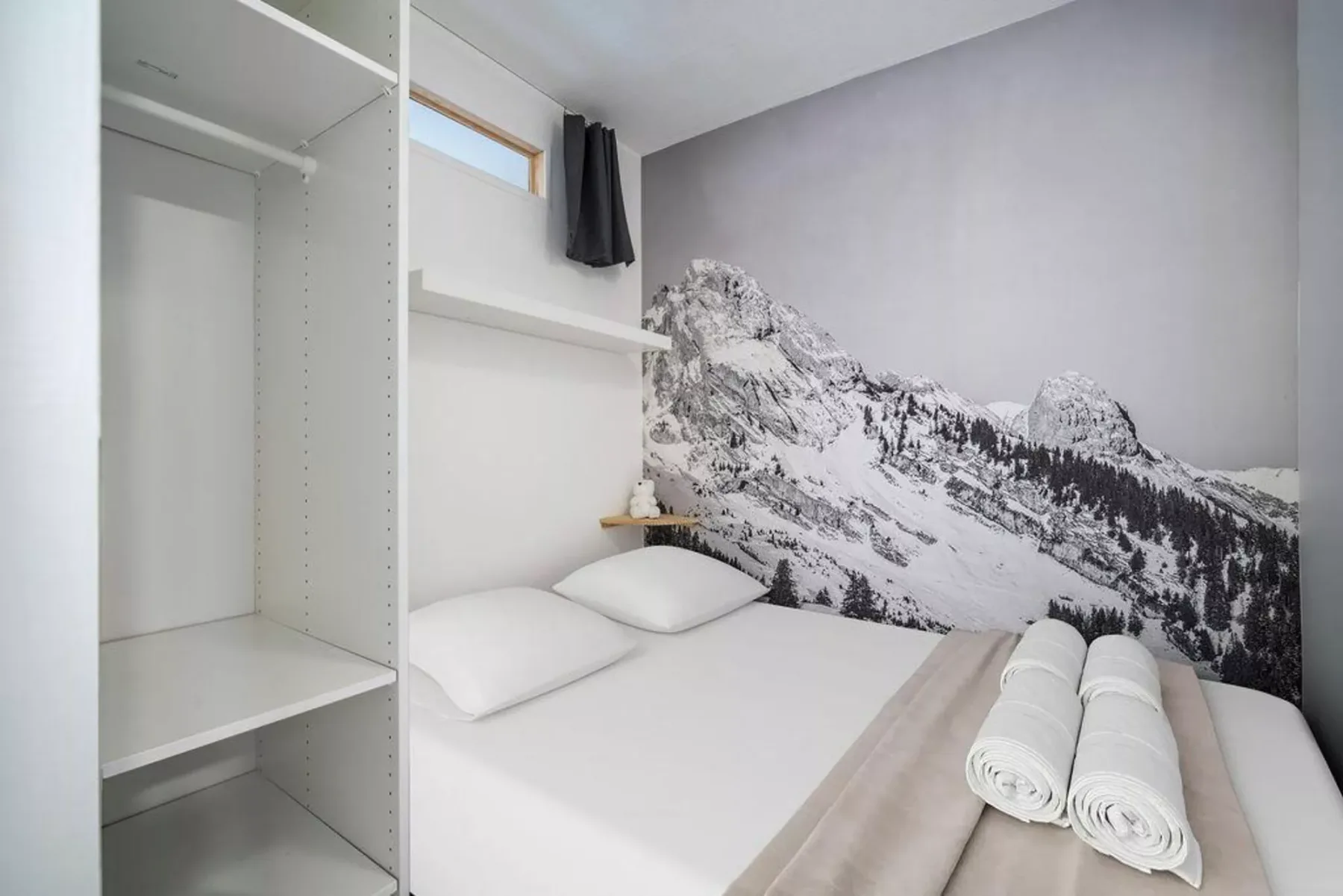 Un dormitorio compacto con una cama frente a un mural de montañas.