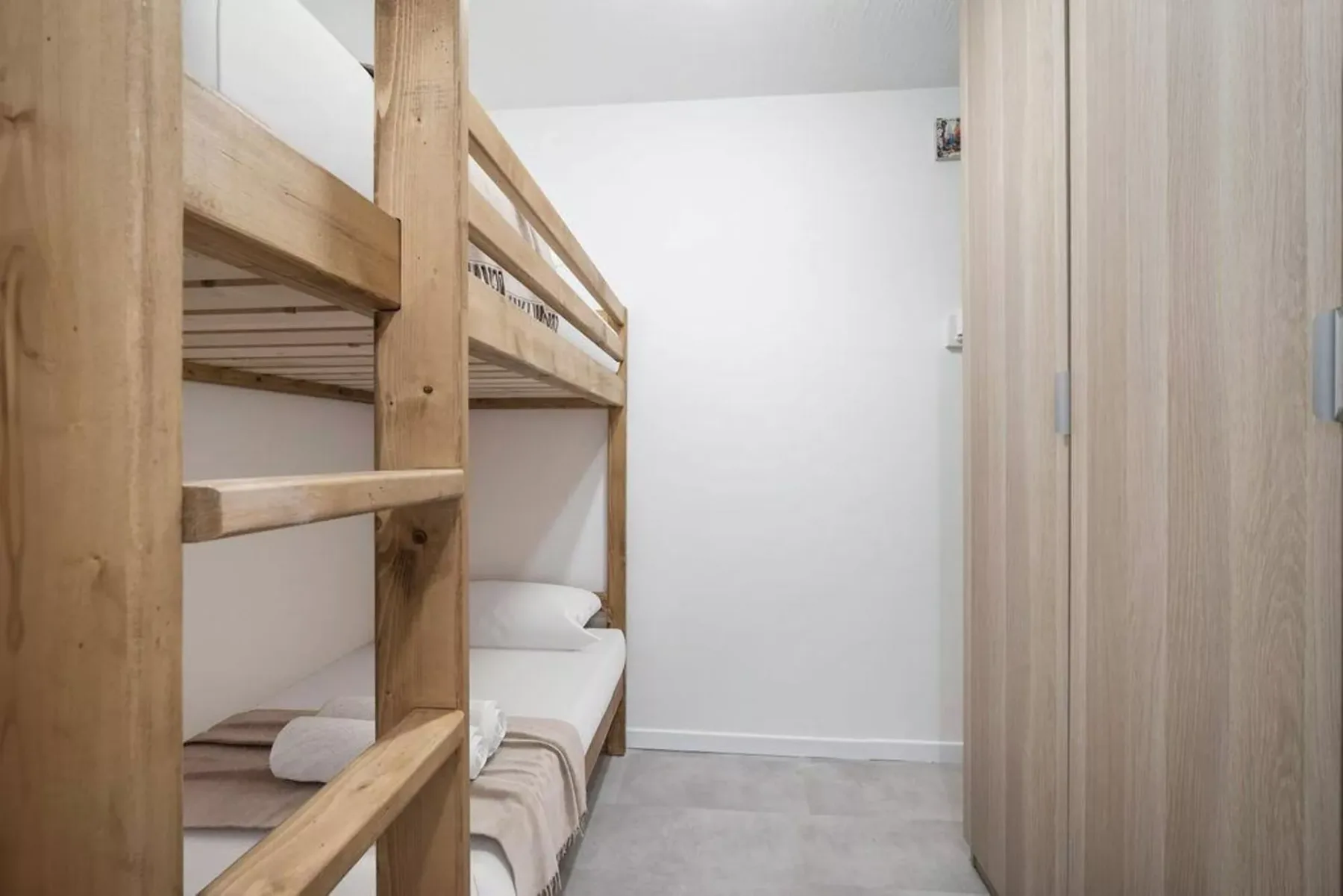 Una litera con ropa de cama blanca está junto a un armario de madera clara.