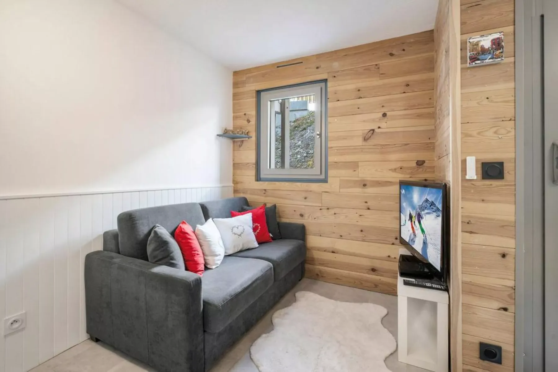 Una pequeña sala de estar con un sofá gris junto a una pared revestida de madera.