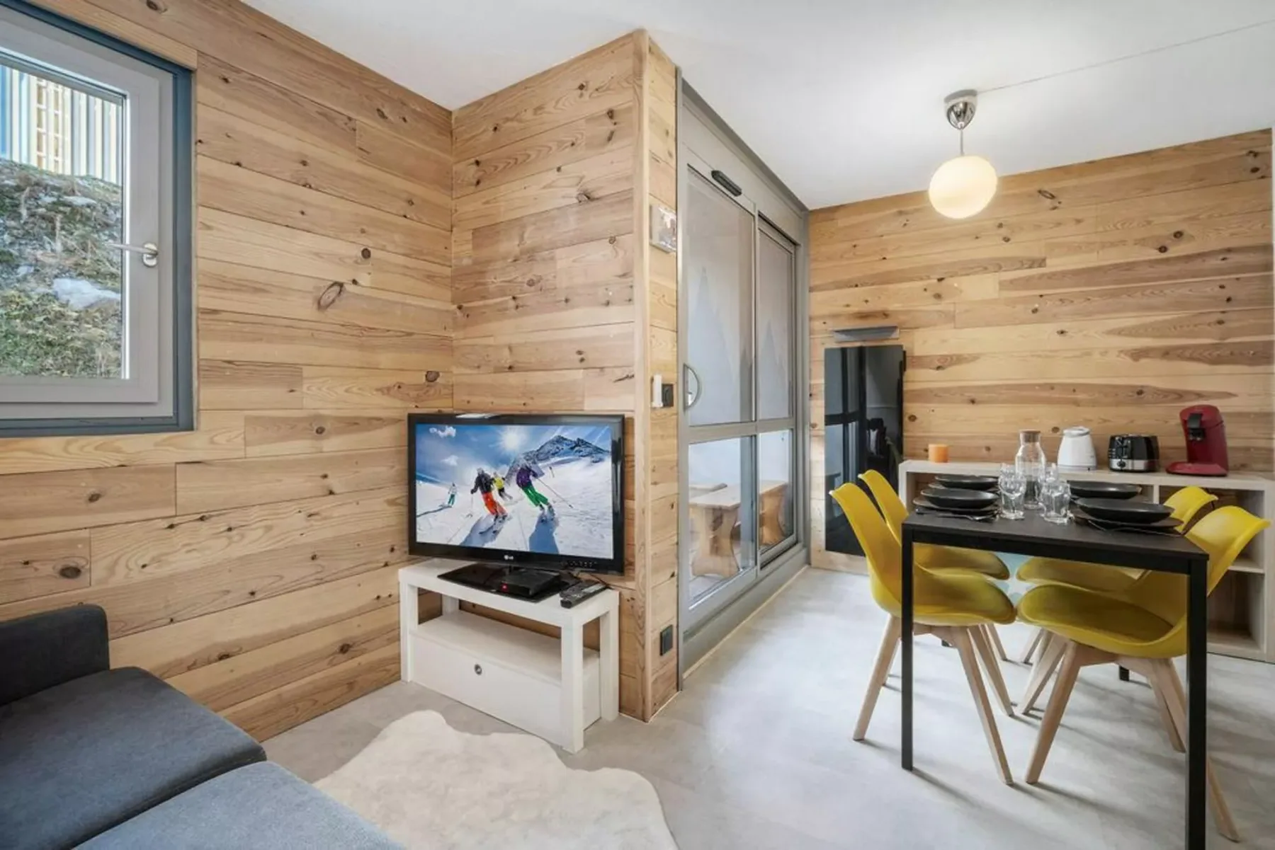 Una sala y comedor revestidos de madera, con un televisor y una mesa preparada para comer.
