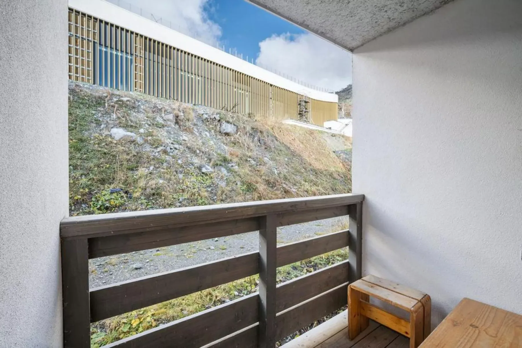 Una zona exterior cubierta con asientos da a una ladera con hierba y un edificio alargado.