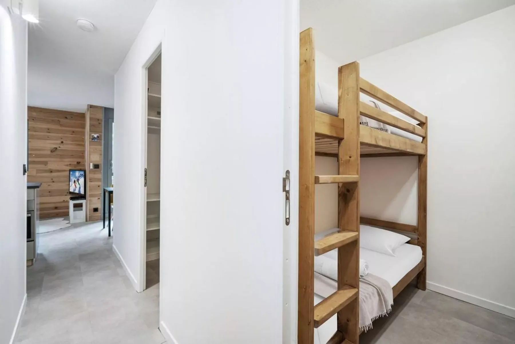 Un dormitorio luminoso con literas de madera junto a un pasillo blanco.