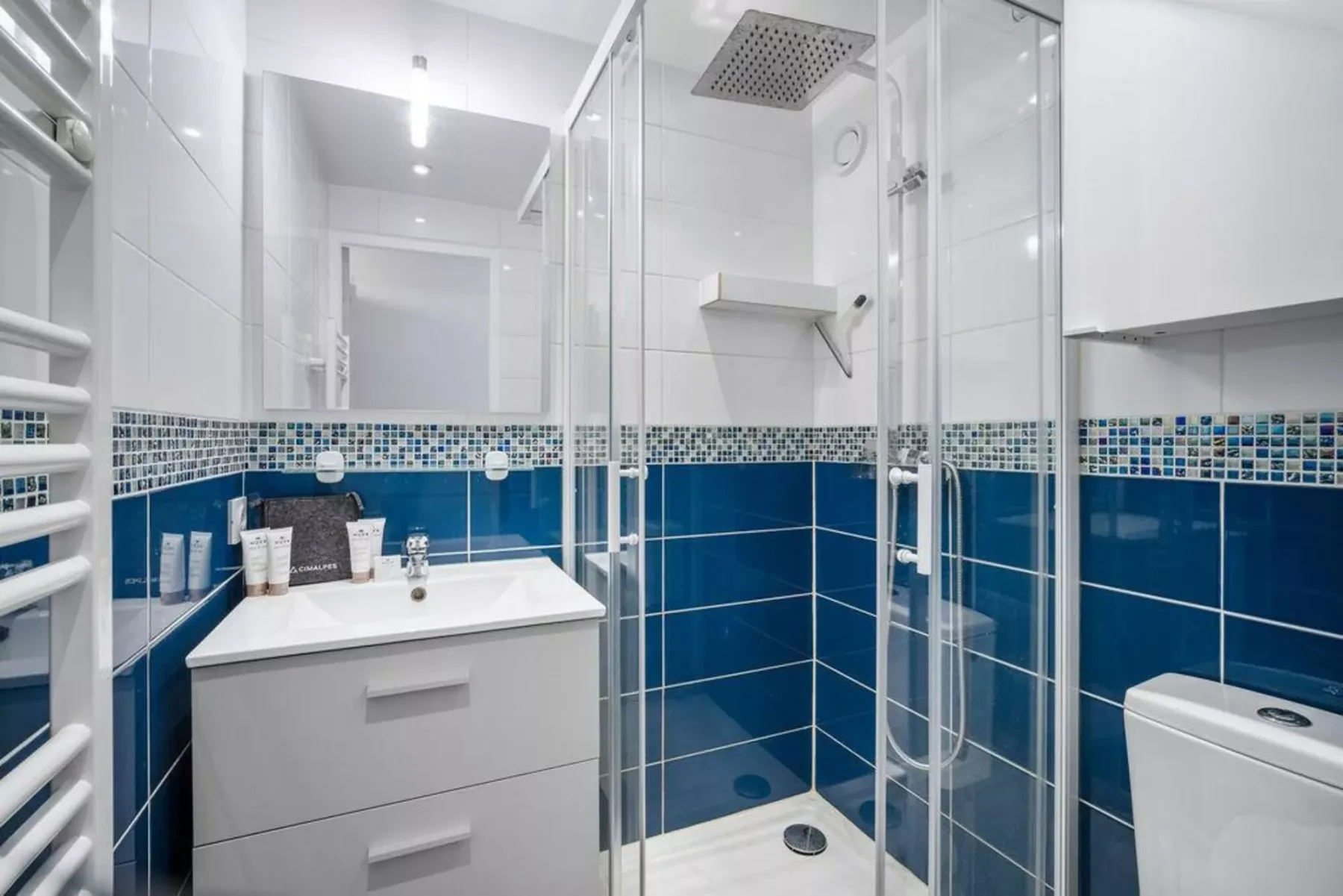 Un baño alicatado con ducha de cristal y mueble con lavabo.