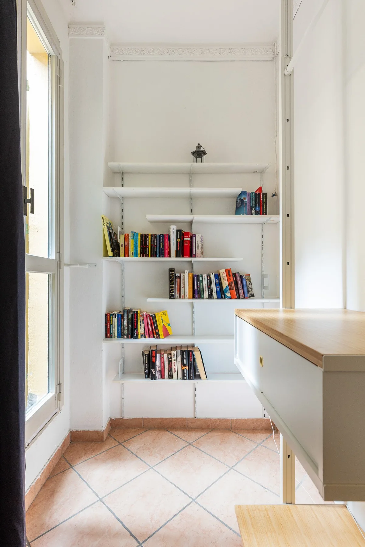 Una habitación luminosa con estantes empotrados llenos de libros junto a una ventana alta.