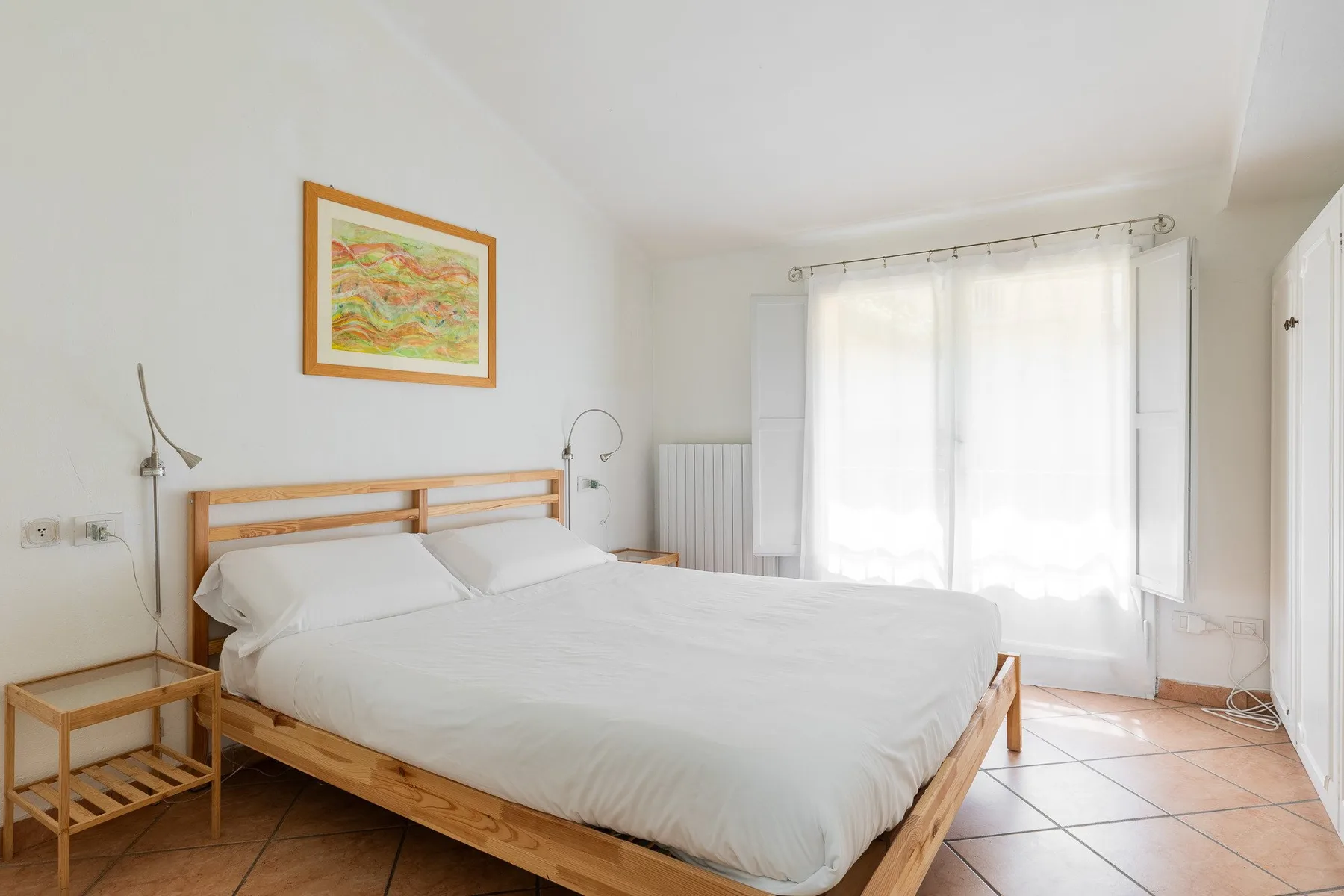 Un dormitorio luminoso con una cama de madera bajo un cuadro enmarcado.
