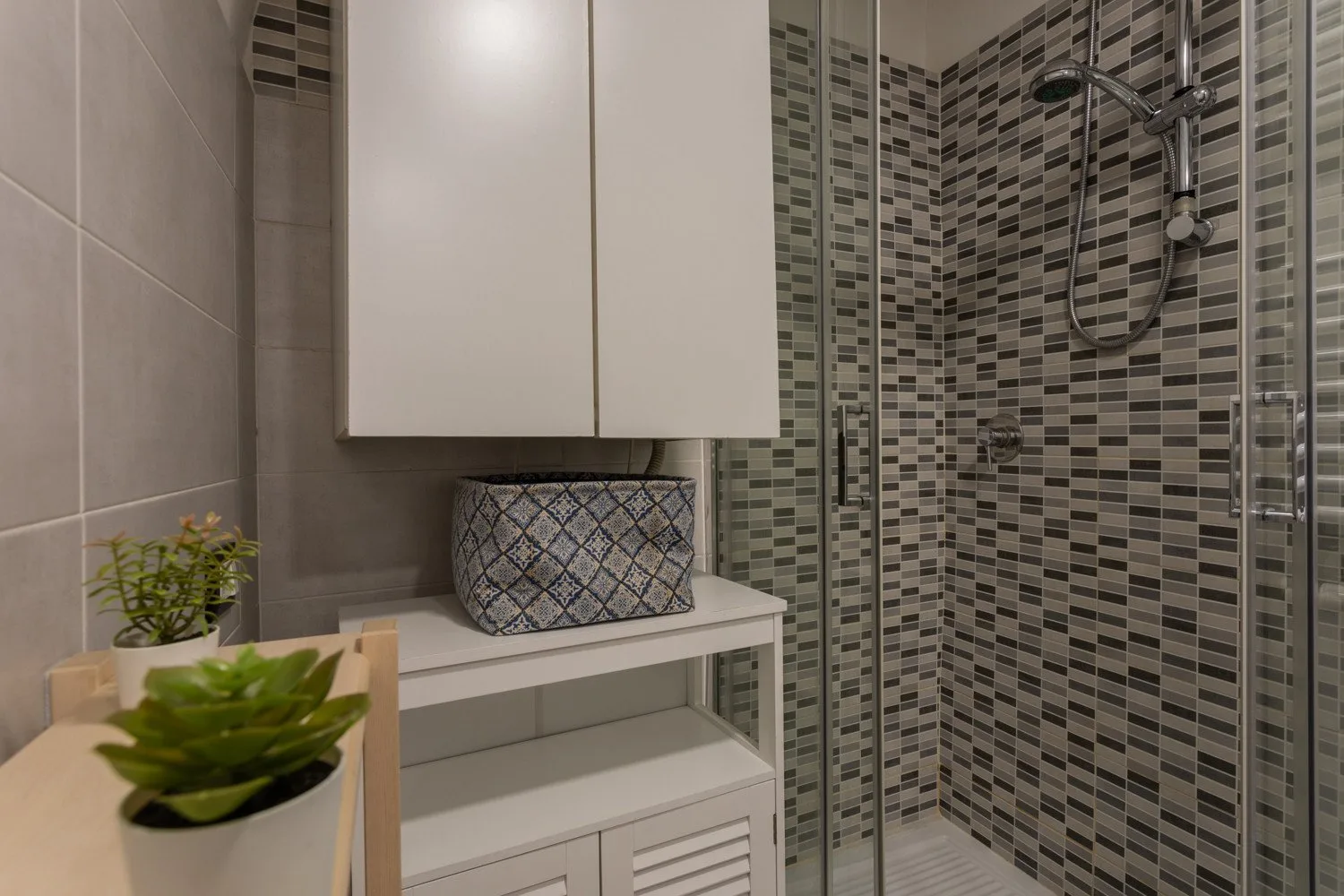 A tiled bathroom with a glass shower and a small vanity.