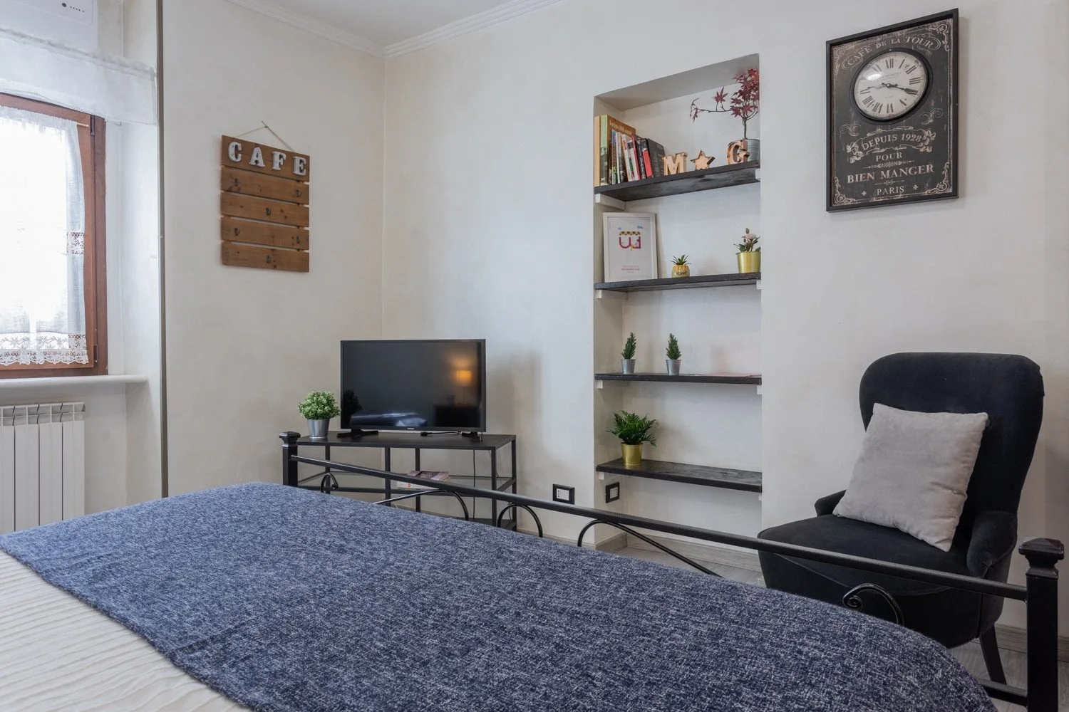 A bedroom with a bed, television, and shelving beside a window.