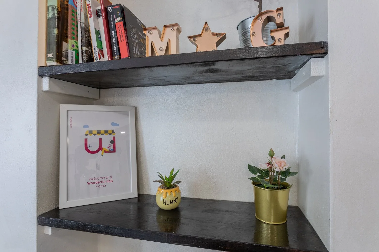 A decorative wall shelving area displays books, framed artwork, and small potted plants.