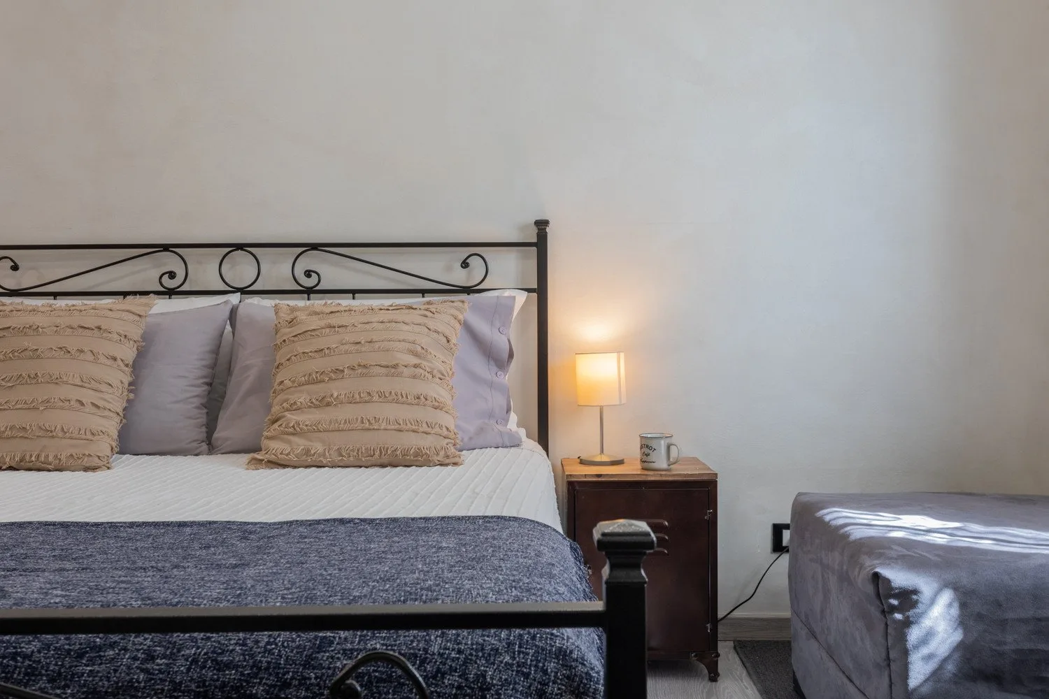A bedroom with a bed, bedside table, and a lit lamp.