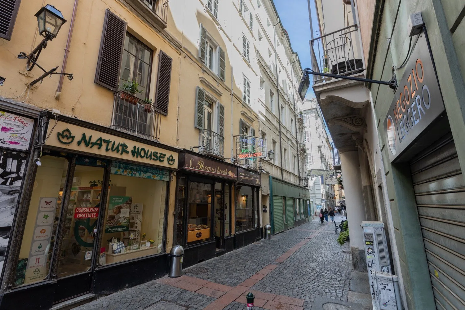 A narrow cobblestone street lined with multistory buildings and storefronts.