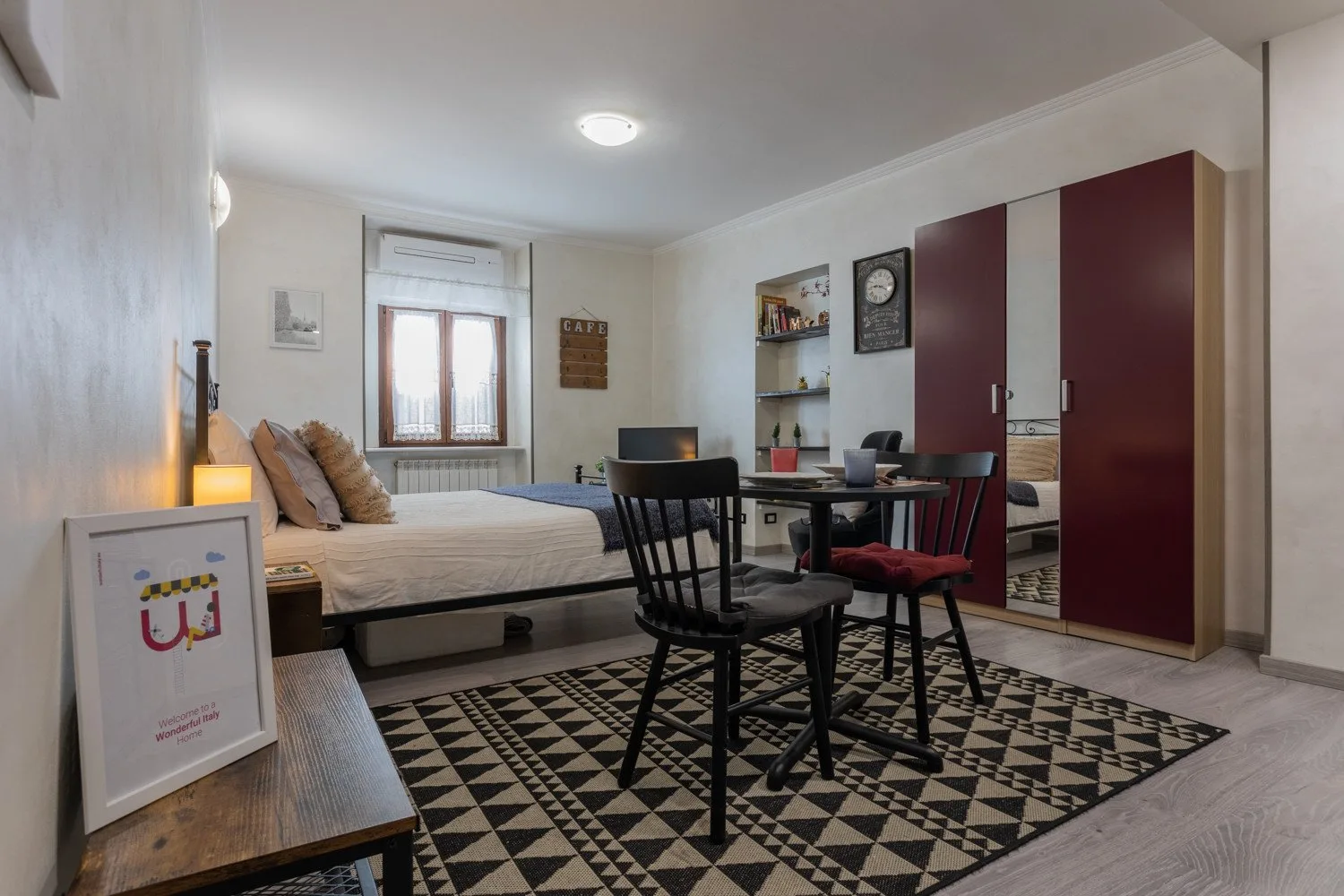 A bedroom with a bed, a dining table, and a black-and-white patterned rug.