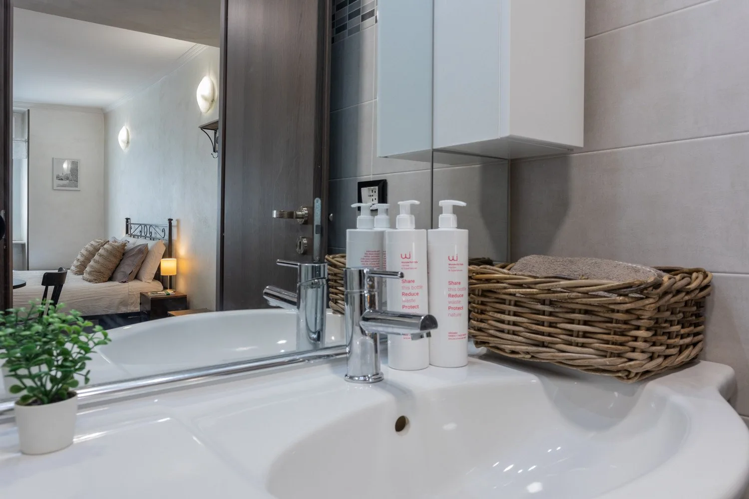 A bathroom sink and mirror are shown, with toiletries and a woven basket beside the basin.