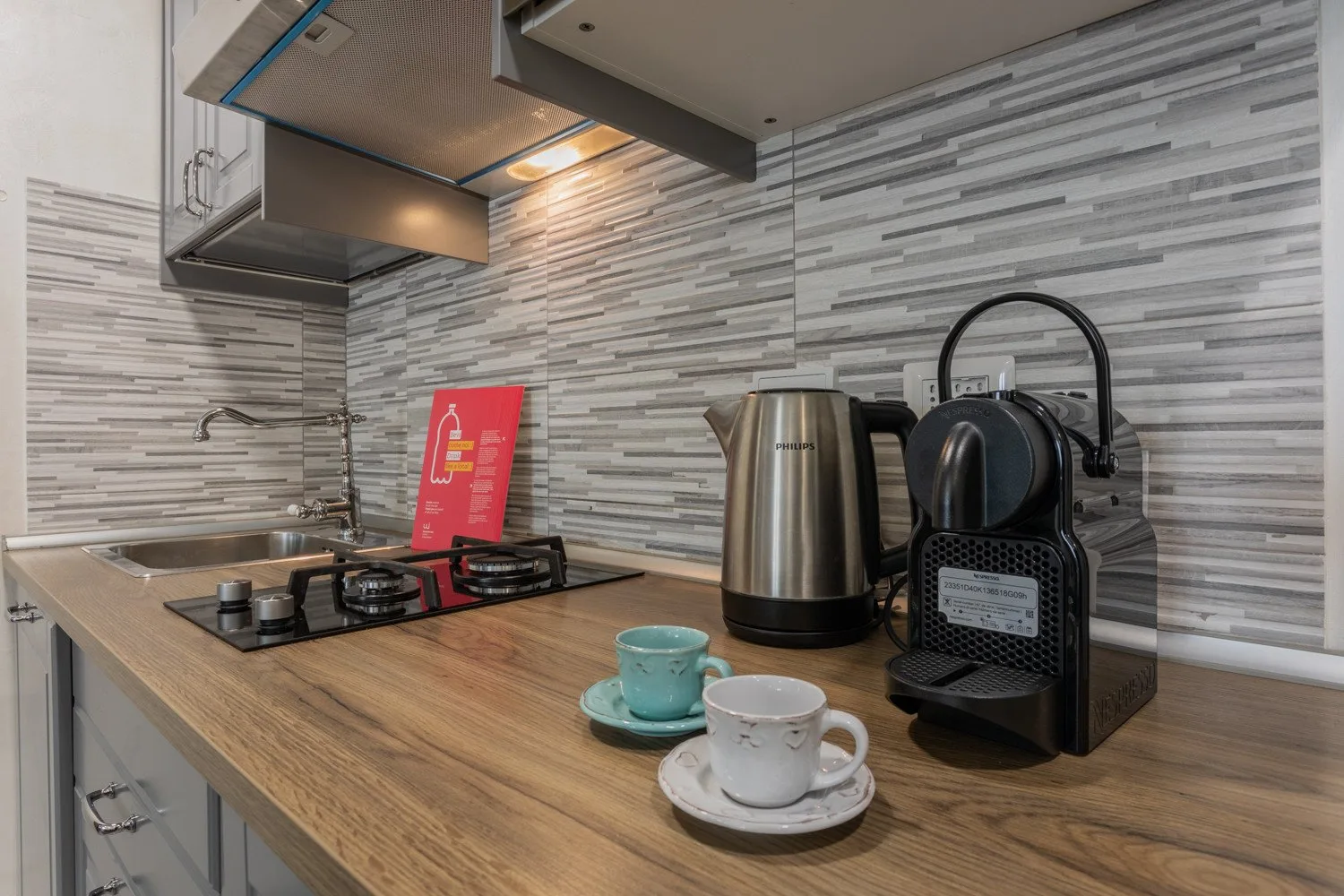 A compact kitchen counter with a sink, stovetop, kettle, and coffee machine.